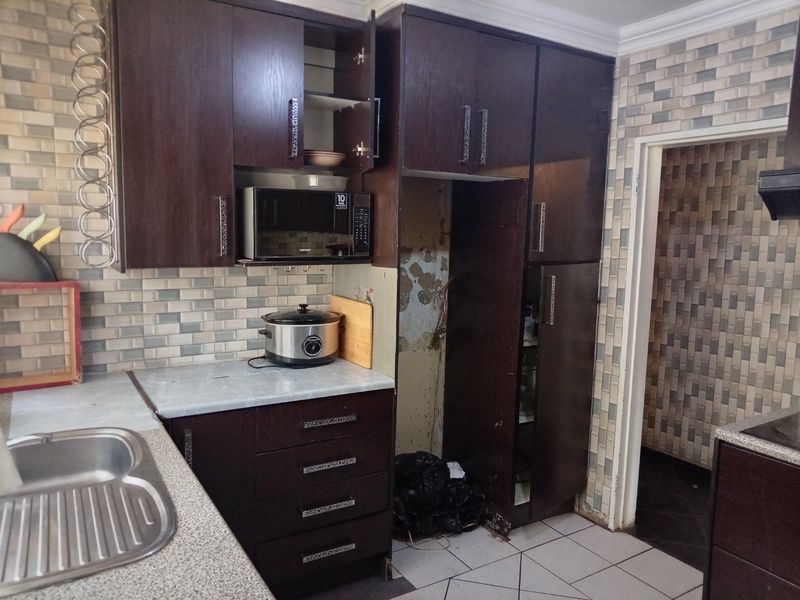 Kitchen featuring dark wood cabinetry, tiled backsplash, and double bowl sink, requiring maintenance and repair to the wall area behind the refrigerator space.
