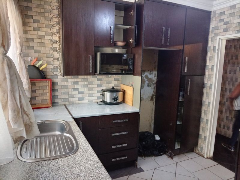 Kitchen featuring dark wood cabinetry, laminate countertops, and a tiled backsplash, requiring some maintenance and repair to the wall area.