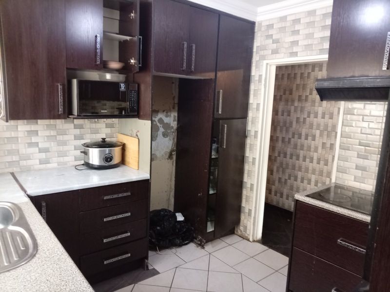 Kitchen featuring dark wood cabinetry, subway tile backsplash, built-in appliances, and tiled flooring, requiring some maintenance and repair to the wall area.