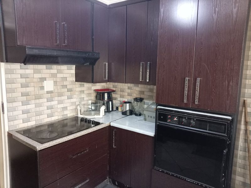 A functional kitchen featuring dark wood cabinetry, a built-in oven, electric hob, extractor fan, and a neutral tiled backsplash.