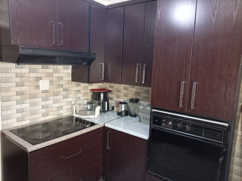 A functional kitchen featuring dark wood cabinetry, a built-in oven, electric cooktop, extractor fan, and a modern subway tile backsplash.