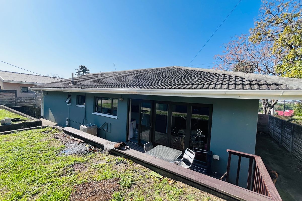 Rear view of the house featuring a tiled roof, sliding glass doors leading to a timber deck, and a tiered garden area.
