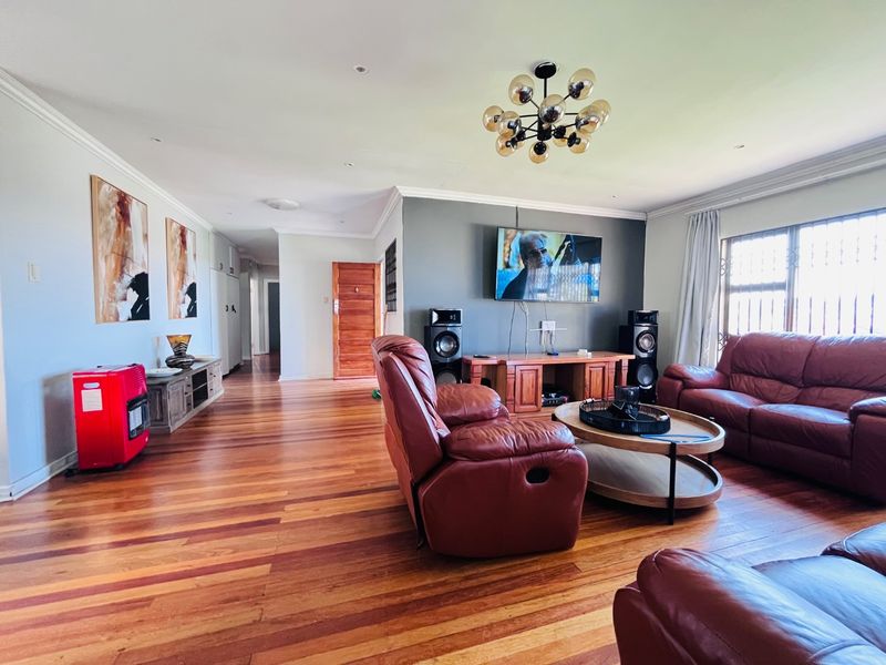 Spacious living room featuring polished hardwood flooring, recessed lighting, a decorative chandelier, and a feature wall with built-in cabinetry and security window grilles.