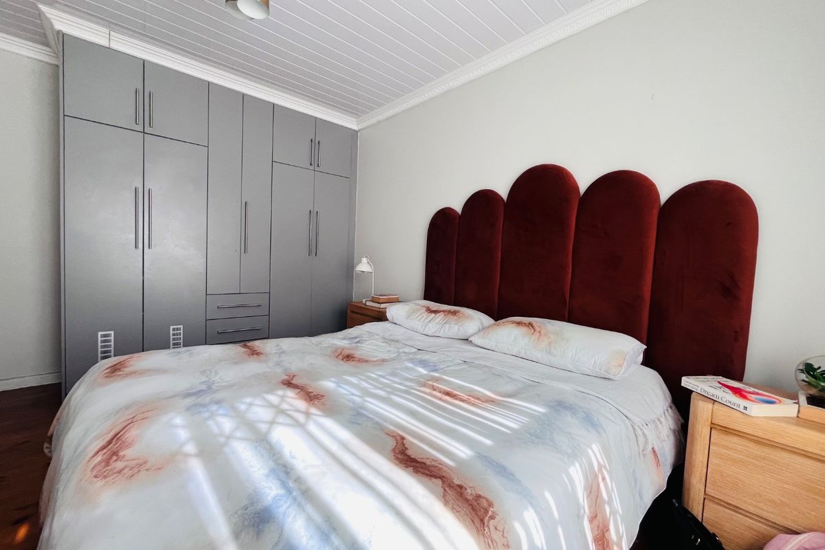 A well-maintained bedroom featuring built-in grey cabinetry, a decorative tongue and groove ceiling with crown molding, and warm hardwood flooring.