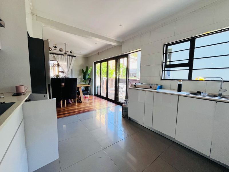 Open-plan kitchen and dining area featuring modern white cabinetry, tiled and wooden flooring, and large sliding doors leading to an outdoor patio.