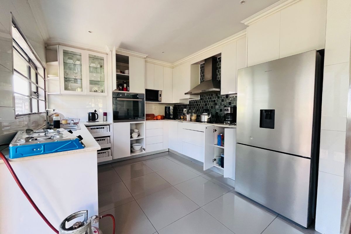 Modern kitchen featuring white cabinetry, tiled backsplash, built-in oven, and extractor fan, with large format floor tiles throughout.