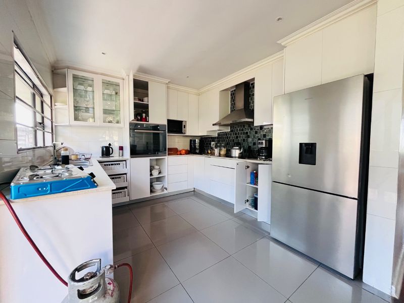 Modern kitchen featuring white cabinetry, tiled backsplash, built-in oven, and extractor fan, with large format floor tiles throughout.