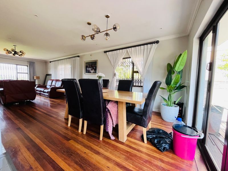 Spacious open-plan living and dining area featuring rich hardwood flooring, abundant natural light from sliding glass doors, and contemporary pendant lighting.