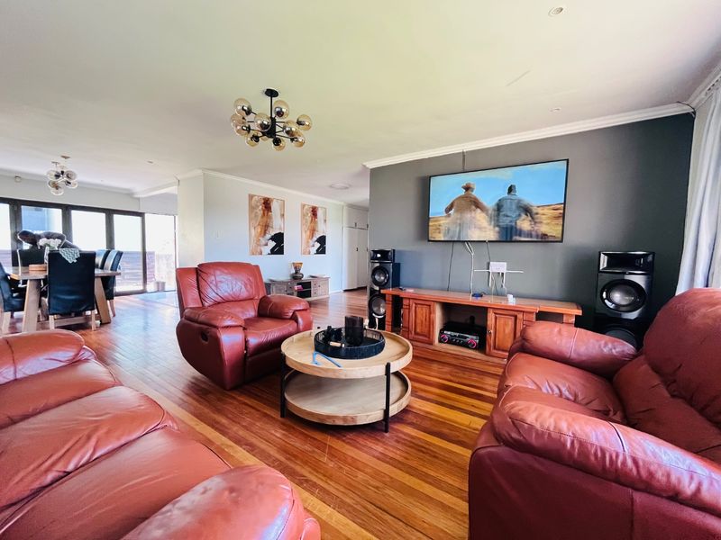 Spacious open-plan living and dining area featuring polished hardwood flooring, crown molding, and contemporary lighting fixtures, creating a warm and inviting atmosphere.
