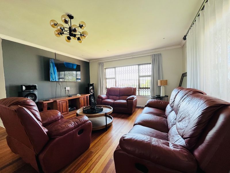 A comfortable living room featuring polished hardwood flooring, crown molding, and large windows fitted with security bars for added peace of mind.