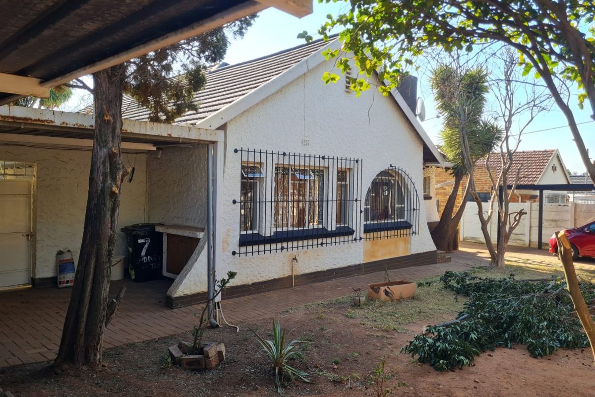 Rear view of the house featuring a covered patio area, paved walkway, and security bars on the windows, set within a garden space.