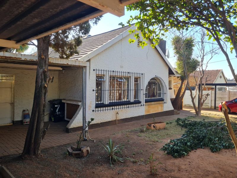 Rear view of the house featuring a covered patio area, paved walkway, and security bars on the windows, set within a garden space.