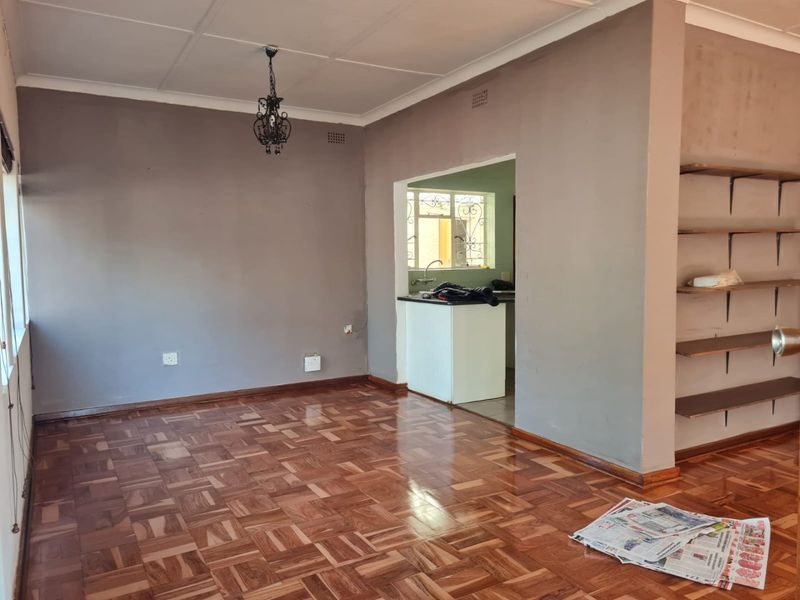 Open plan living area featuring polished parquet flooring, built-in wall shelving, and a convenient pass-through window connecting to the kitchen space.
