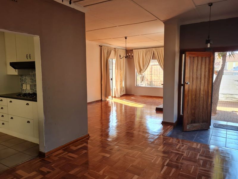 Open-plan living area featuring polished parquet flooring, flowing into a functional kitchen with built-in cabinetry and direct access to the exterior.