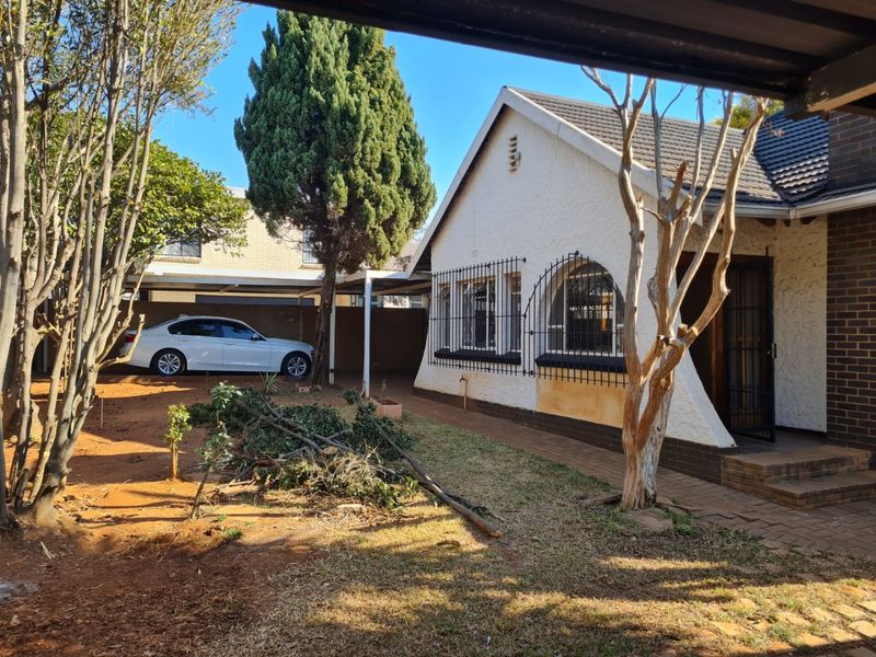 Front view of a house featuring a tiled roof, security bars on windows, and a paved walkway leading to the entrance with an adjacent carport.