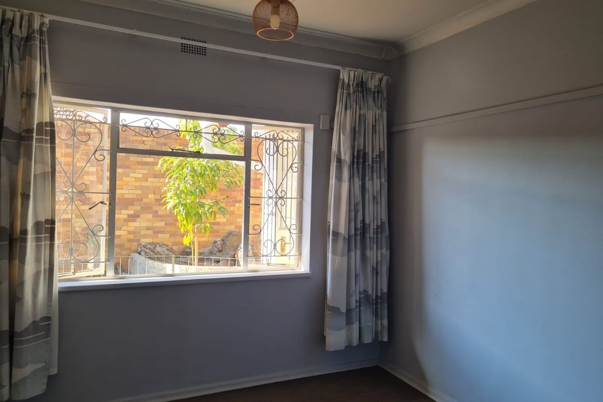 A bright, empty bedroom featuring a large window with decorative security gates, carpeted flooring, and classic picture rail detailing.