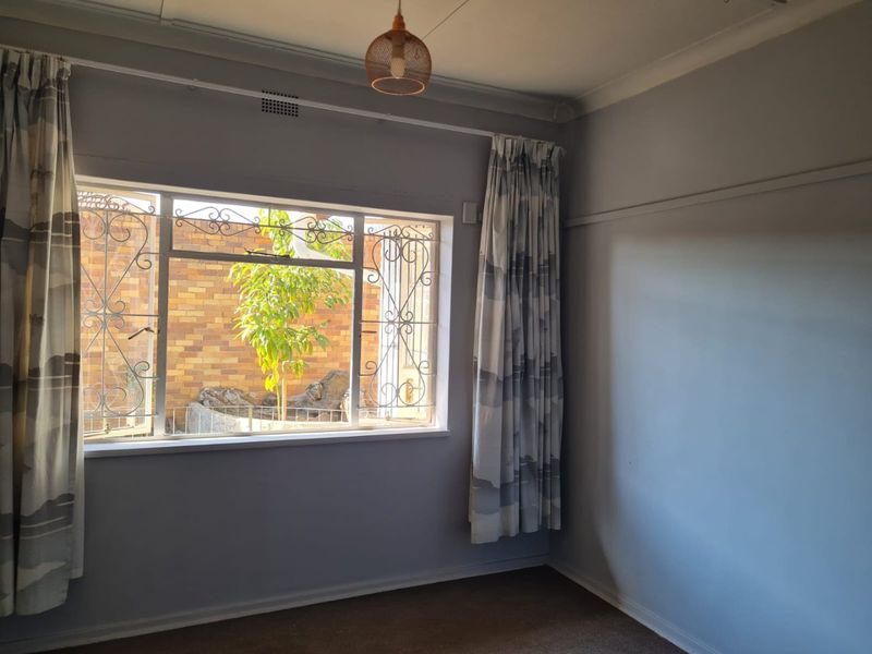 A bright, empty bedroom featuring a large window with decorative security gates, carpeted flooring, and classic picture rail detailing.