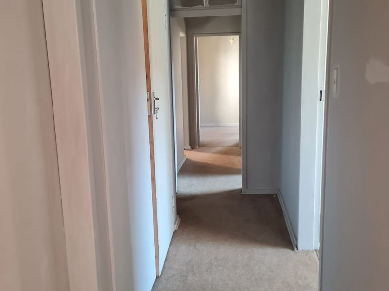 A vacant hallway featuring built-in cupboards, carpeted flooring, and a transom window, connecting multiple rooms within the home.
