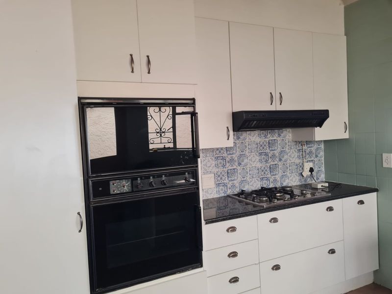 A functional kitchen featuring white cabinetry, a granite countertop, a built-in oven, and a gas hob with a decorative patterned tile backsplash.