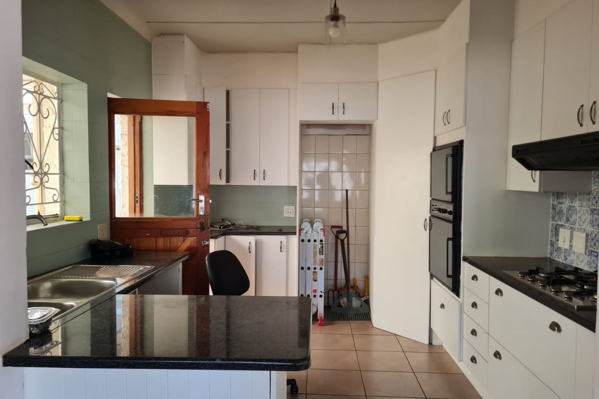 Functional kitchen featuring white cabinetry, granite countertops, built-in double oven, gas hob, and tiled flooring with direct access to the exterior.