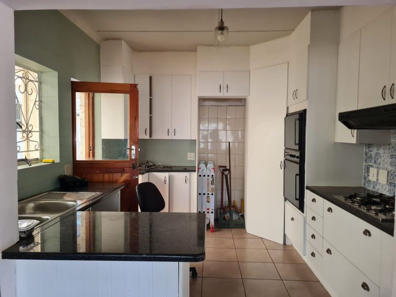 Functional kitchen featuring white cabinetry, granite countertops, built-in double oven, gas hob, and tiled flooring with direct access to the exterior.