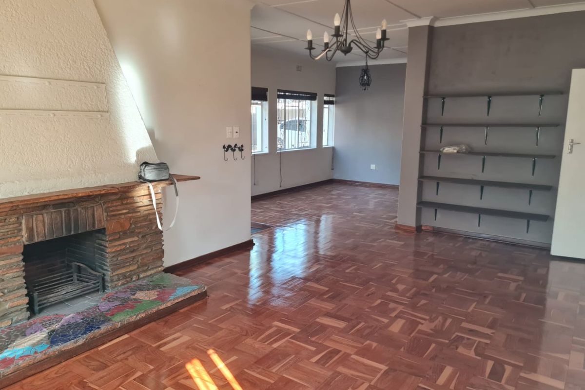 Spacious living area featuring classic parquet flooring, a prominent brick fireplace, and built-in shelving, offering a versatile layout for comfortable family living.