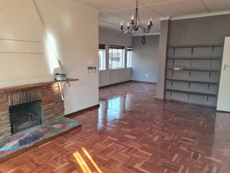 Spacious living area featuring classic parquet flooring, a prominent brick fireplace, and built-in shelving, offering a versatile layout for comfortable family living.