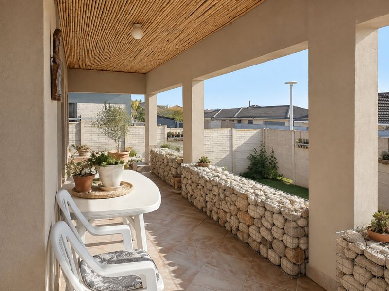 A covered patio featuring a unique bamboo ceiling, tiled flooring, and decorative gabion stone walls, overlooking a private rear garden area.