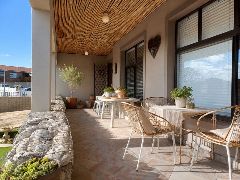 A covered patio area featuring a unique bamboo ceiling, tiled flooring, and a decorative gabion stone wall, providing a pleasant outdoor living space.