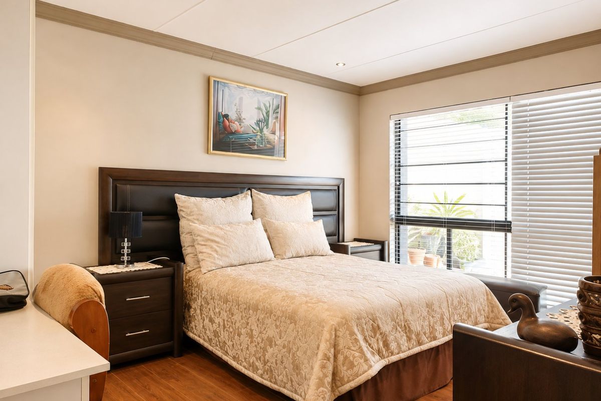 A well-maintained bedroom featuring laminate flooring, recessed downlighting, and venetian blinds, offering a comfortable and neutral living space.