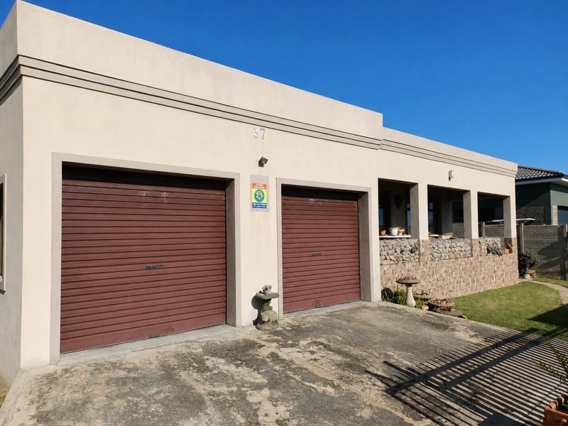 Front view of a residential property featuring a double garage with roller shutter doors, stone cladding accents, and a covered porch area.