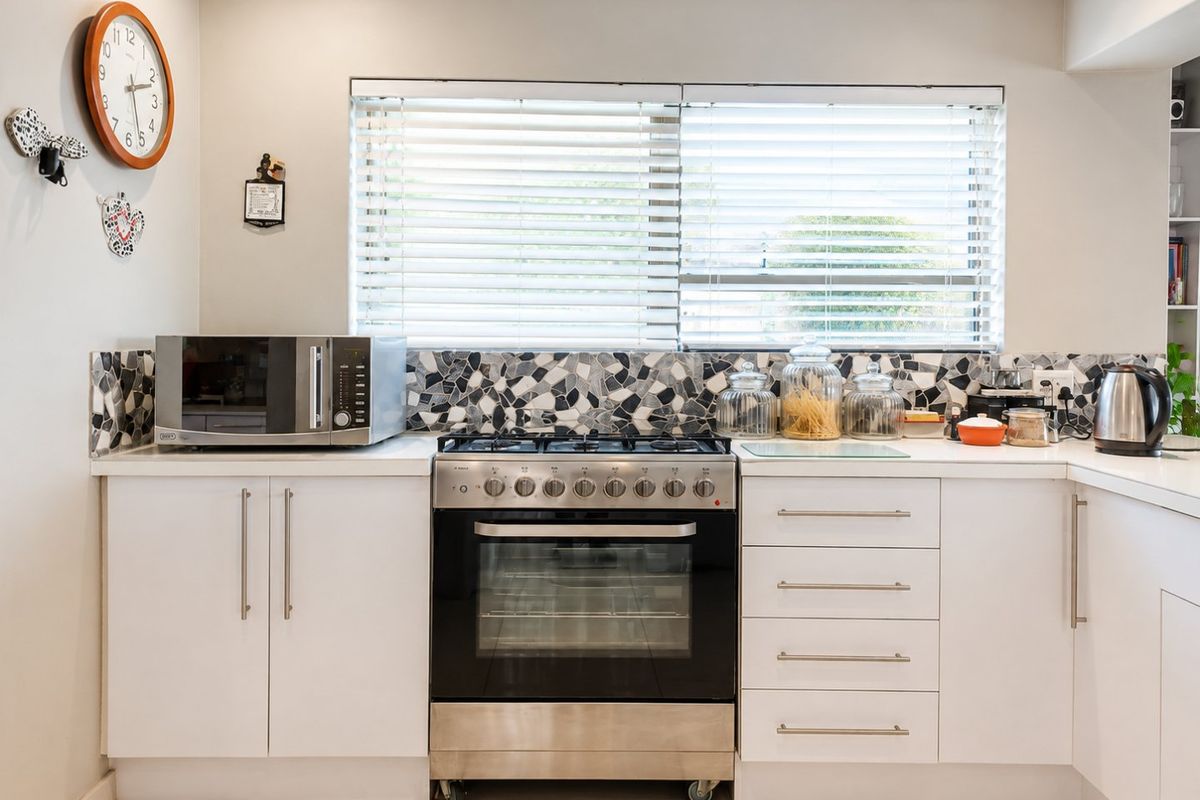 A clean, modern kitchen featuring white cabinetry, a stainless steel gas stove with oven, and a decorative mosaic tile backsplash.