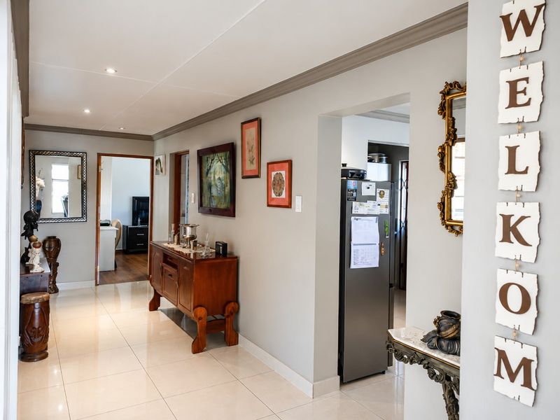 A bright and well-maintained hallway featuring neutral tiled flooring, recessed lighting, and coved ceiling cornices, providing access to adjacent living and kitchen areas.