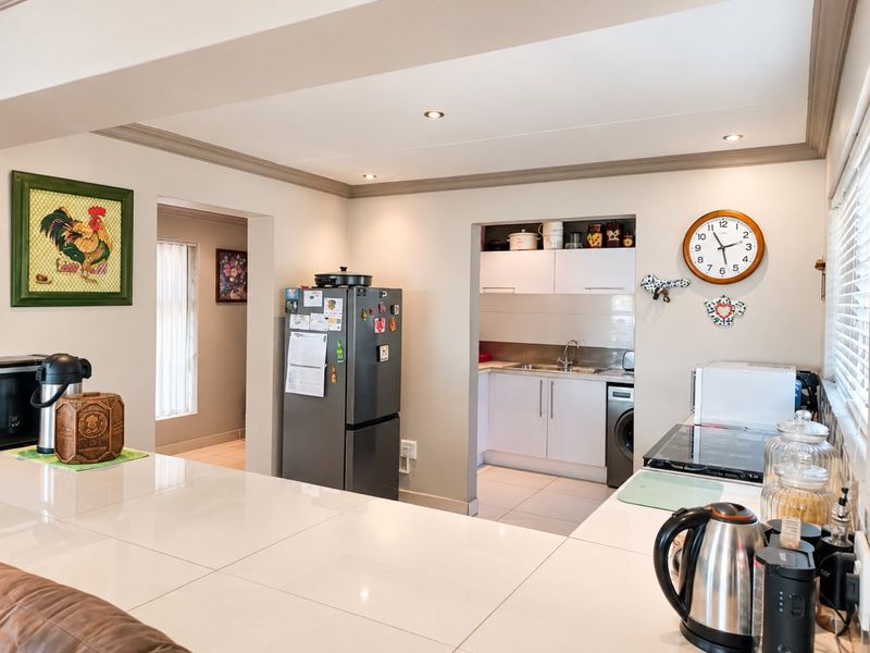 Open-plan kitchen area featuring tiled flooring, recessed lighting, and a functional scullery nook with built-in cabinetry and sink.