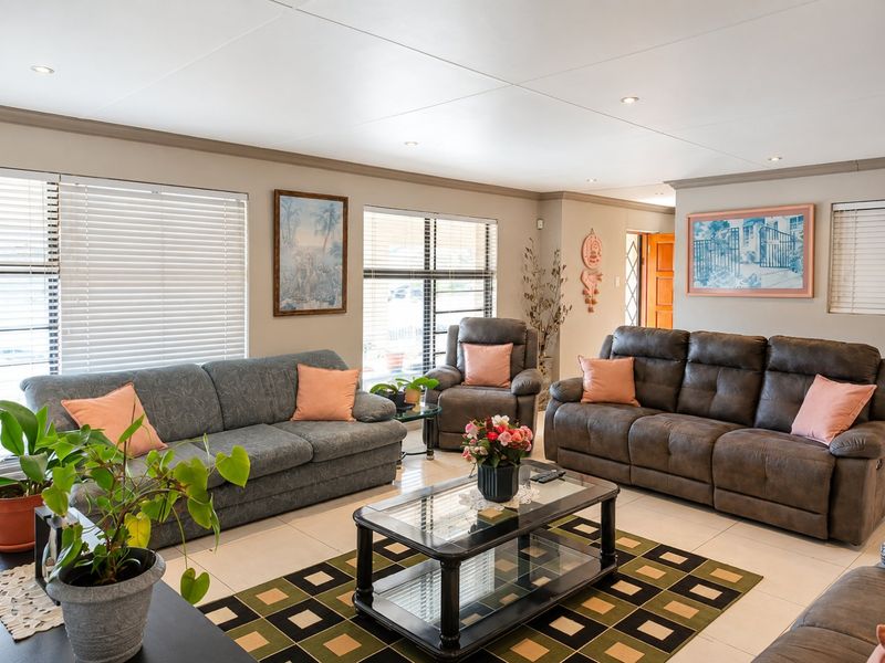 A well-maintained living room featuring neutral tiled flooring, recessed downlighting, and large windows fitted with venetian blinds.