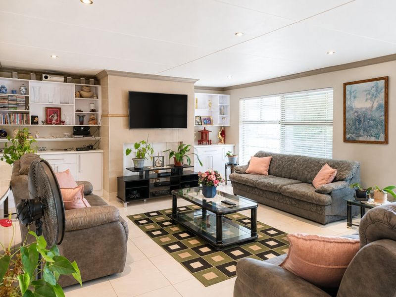 Spacious living room featuring neutral tiled flooring, recessed ceiling lights, and extensive built-in cabinetry for storage and display.