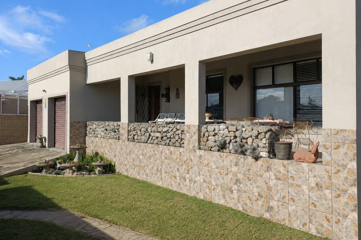 Rear view of the property featuring a covered patio with gabion wall detailing, tiled facade, and access to the garage area.