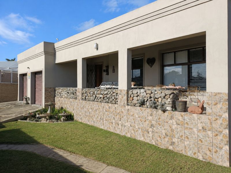 Rear view of the property featuring a covered patio with gabion wall detailing, tiled facade, and access to the garage area.