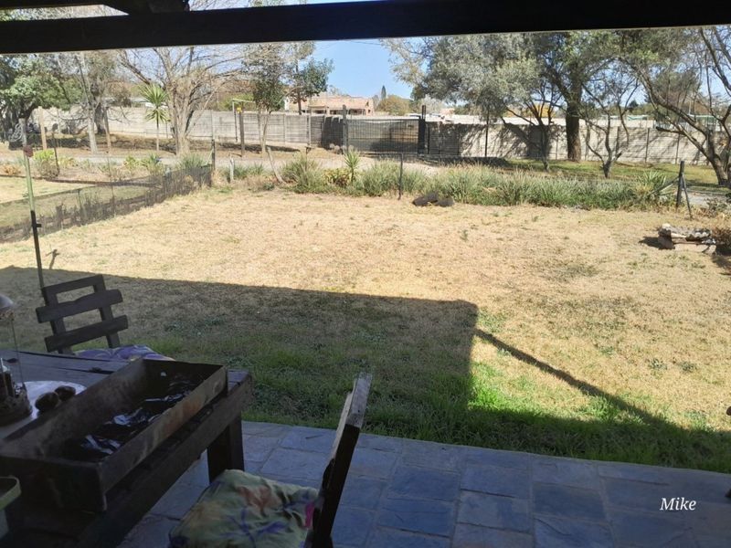 A covered patio area overlooking a large, dry backyard with perimeter fencing and mature trees.