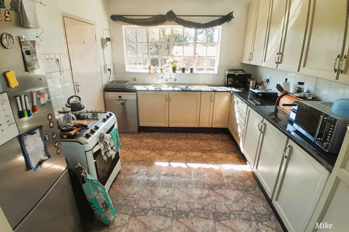 A functional kitchen featuring built-in cabinetry, laminate countertops, a double sink, and tiled flooring, offering a practical layout with natural light.