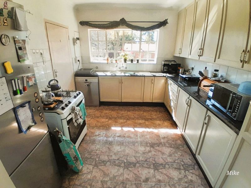 A functional kitchen featuring built-in cabinetry, laminate countertops, a double sink, and tiled flooring, offering a practical layout with natural light.