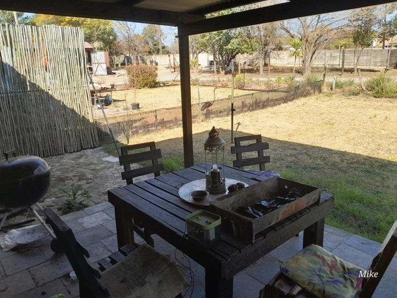 A covered outdoor patio area featuring paved flooring and timber support posts, overlooking a spacious backyard garden.