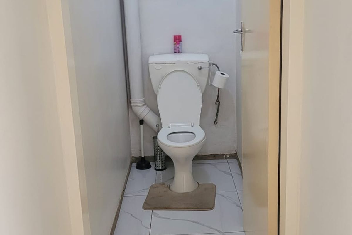 A compact bathroom featuring tiled flooring, a standard toilet, and exposed plumbing infrastructure.