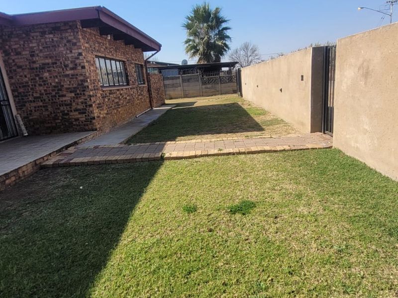 A rear exterior view of the property featuring a face brick facade, a paved walkway, and a private lawn area enclosed by boundary walls.