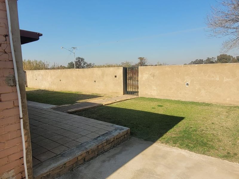 Rear exterior view featuring a tiled patio area, a lawn, and a perimeter wall with a metal gate.