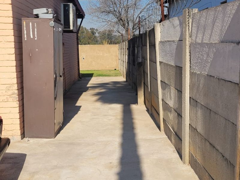 A narrow concrete paved side passage between a brick building and a high boundary wall topped with razor wire.