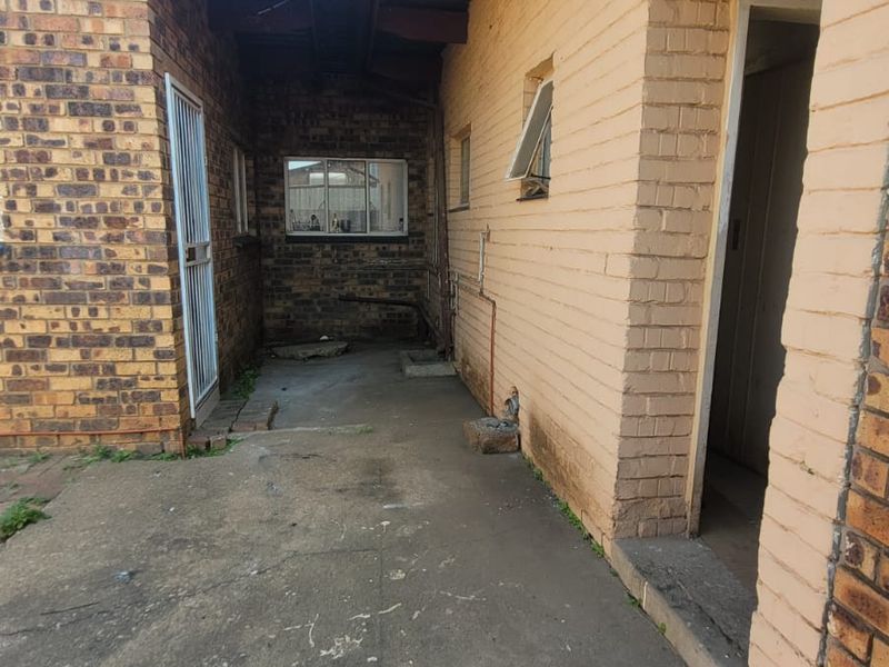 A rear exterior view of the commercial property featuring exposed brick walls, concrete paving, and a covered walkway area.