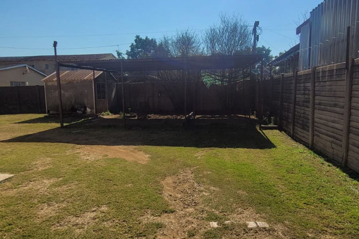 Spacious rear yard featuring a metal carport structure, perimeter precast concrete fencing, and an outbuilding, offering potential for landscaping or outdoor development.