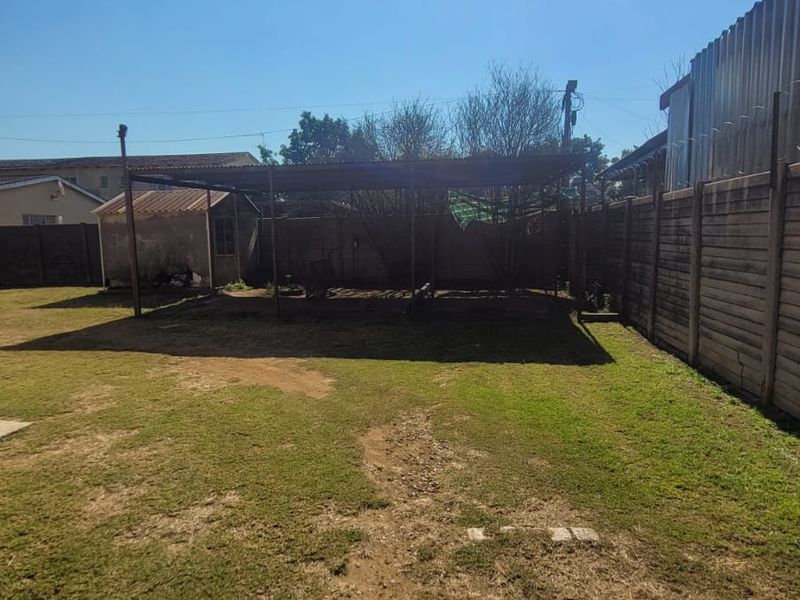 Spacious rear yard featuring a metal carport structure, perimeter precast concrete fencing, and an outbuilding, offering potential for landscaping or outdoor development.