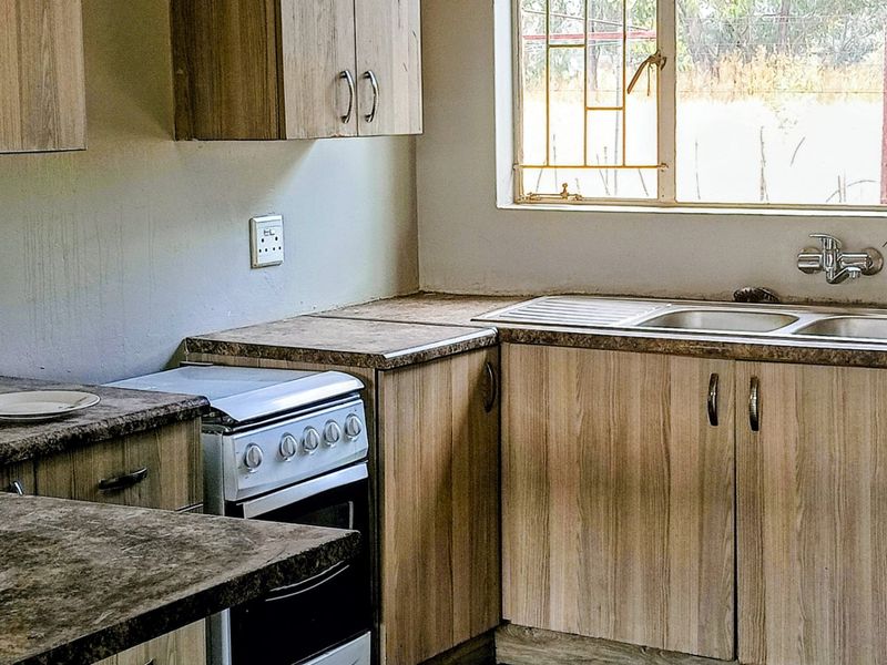 A functional kitchen featuring wood-look laminate cabinetry, laminate countertops, a stainless steel sink, and a freestanding stove with natural light.